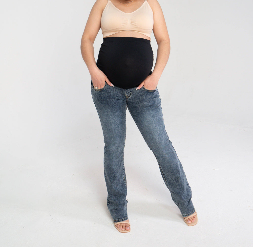 Woman standing with her hands in the pockets of the bootleg maternity jeans, showing the front pockets and the black belly panel
