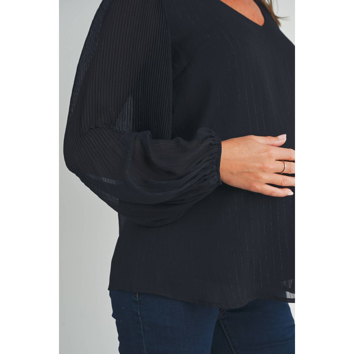 Close-up of the black maternity blouse showing its sheer pleated balloon sleeve and gathered cuff, with a hand resting on the pregnant belly
