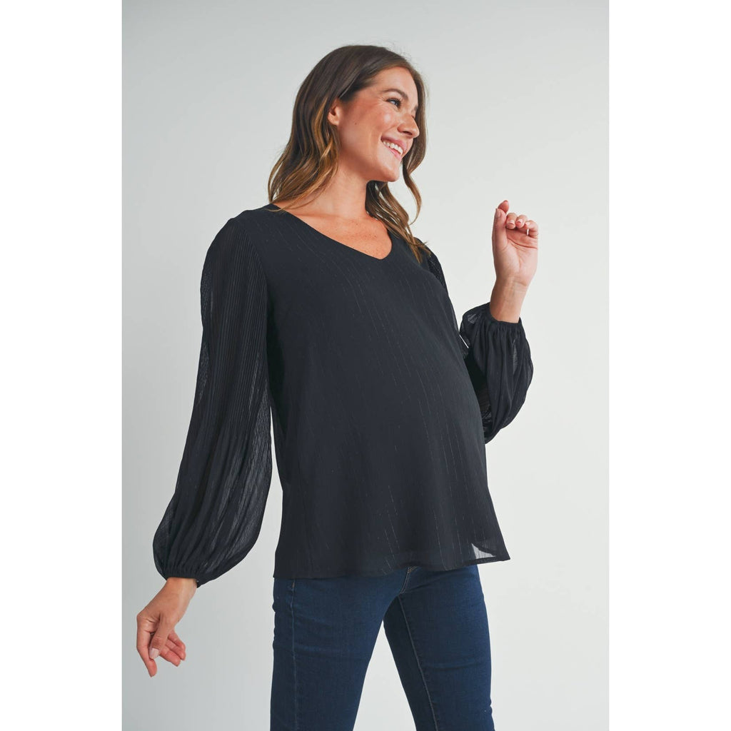 Woman smiling and facing left, wearing the black long sleeve maternity blouse against a light background
