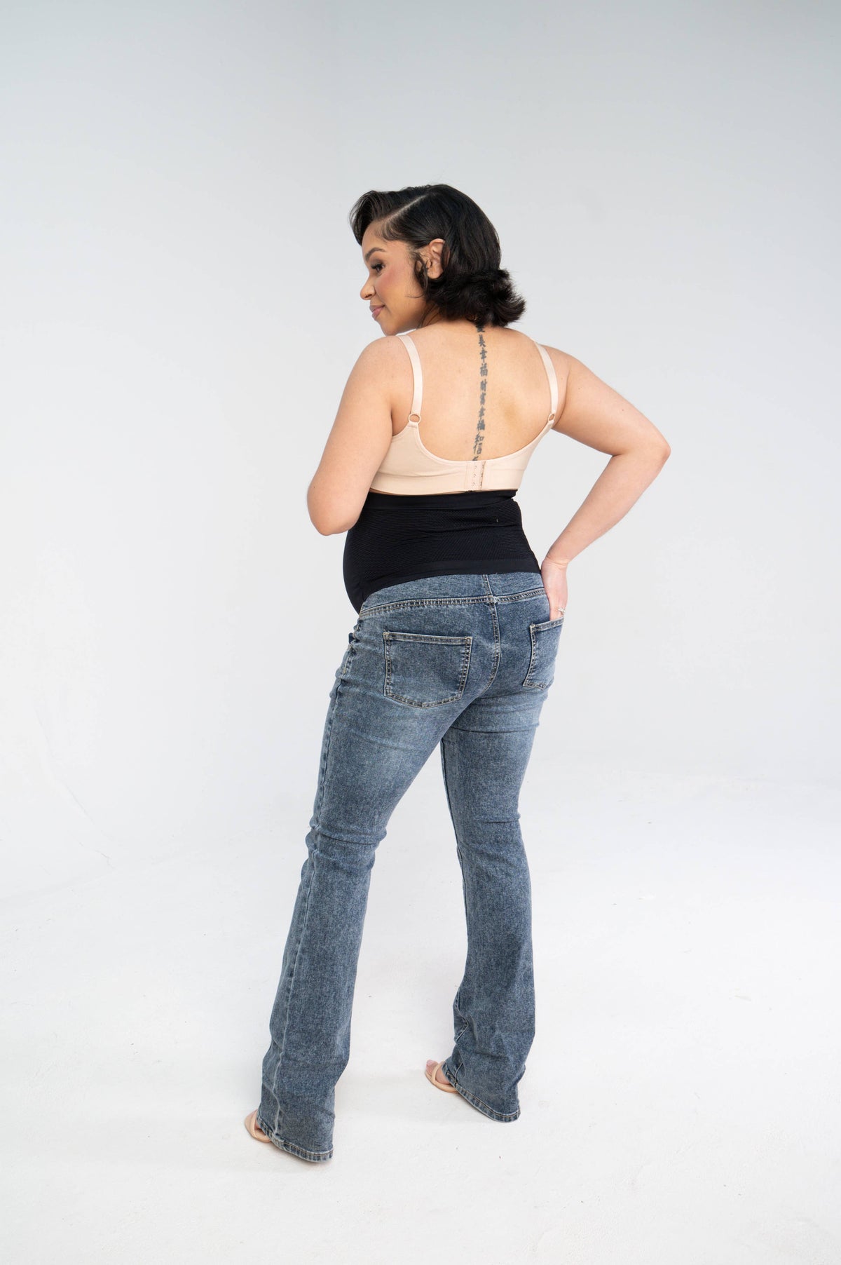 Back view of a pregnant woman wearing the bootleg maternity jeans with the black over-the-belly panel