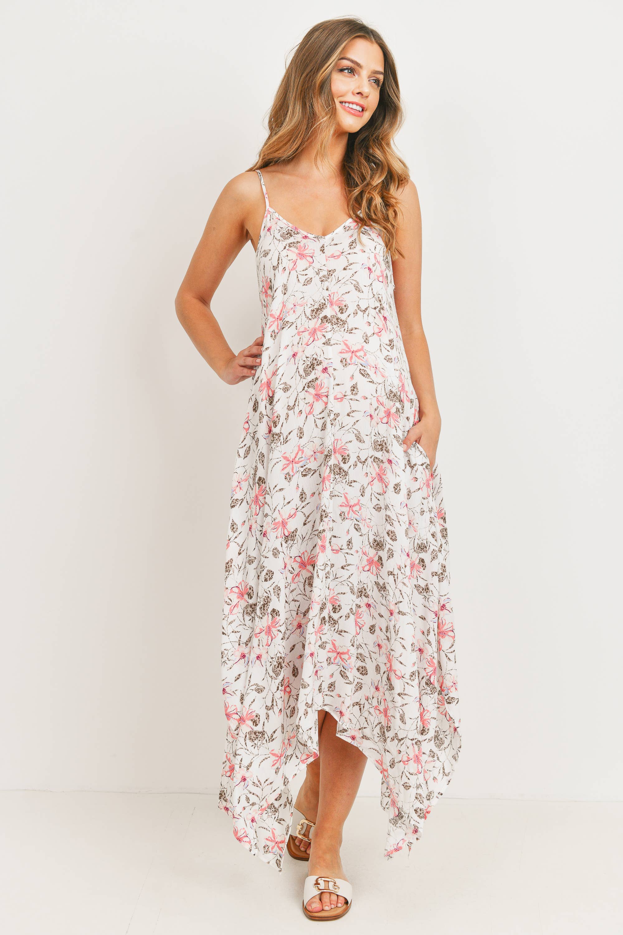 Woman standing against a white background wearing a long maternity dress with a tropical design and pink flowers