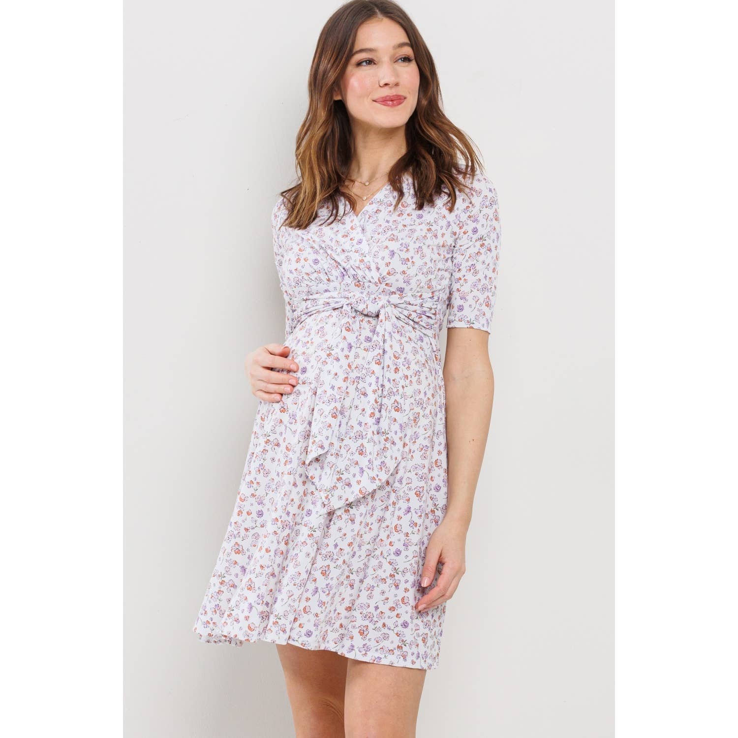Woman wearing a floral maternity dress looking to the right and smiling against a plain background