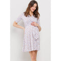 Woman standing against a gray  background, wearing a knee-length maternity dress that has pink and purple flowers