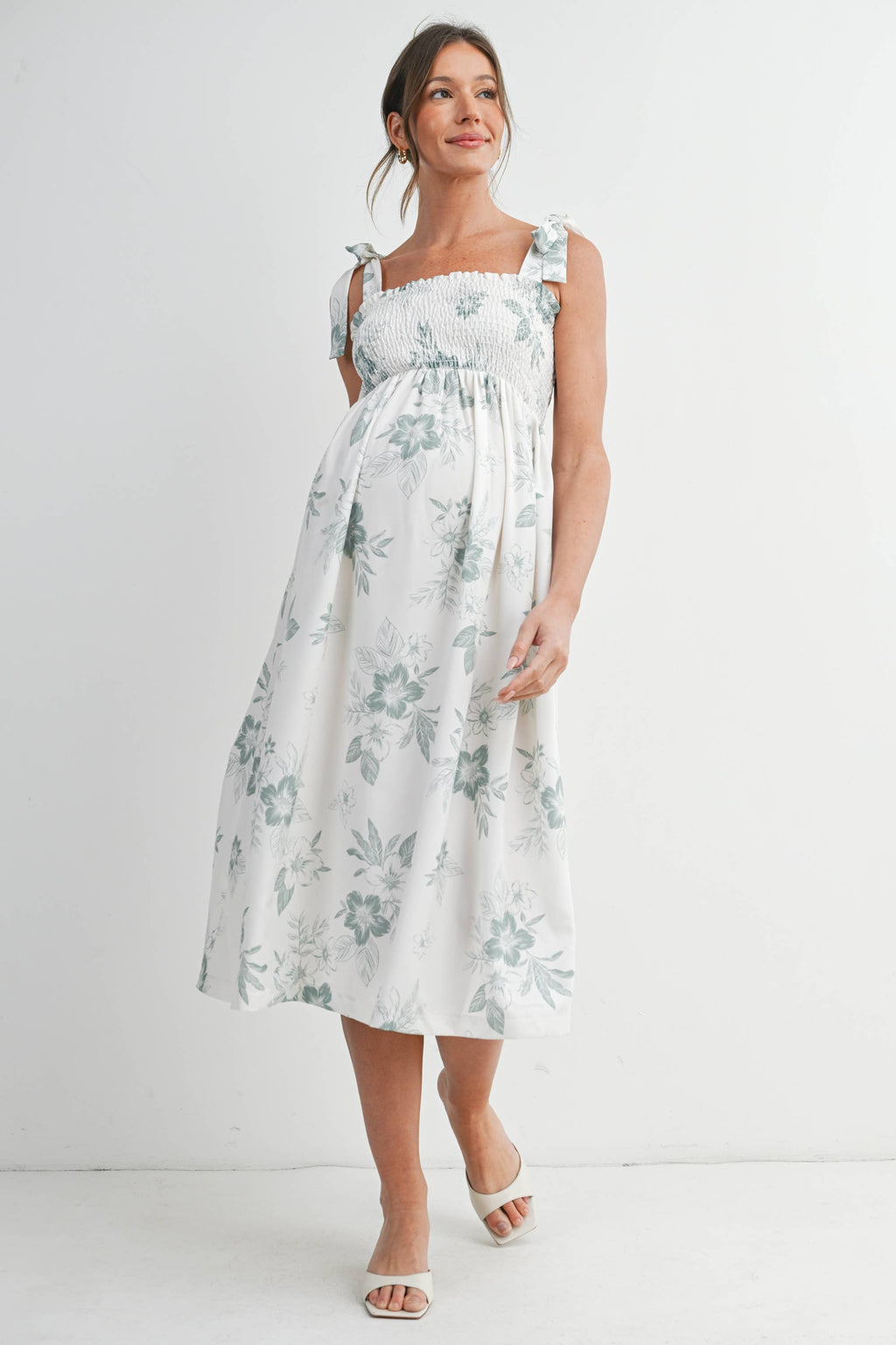 Woman wearing a floral maternity dress against a white background