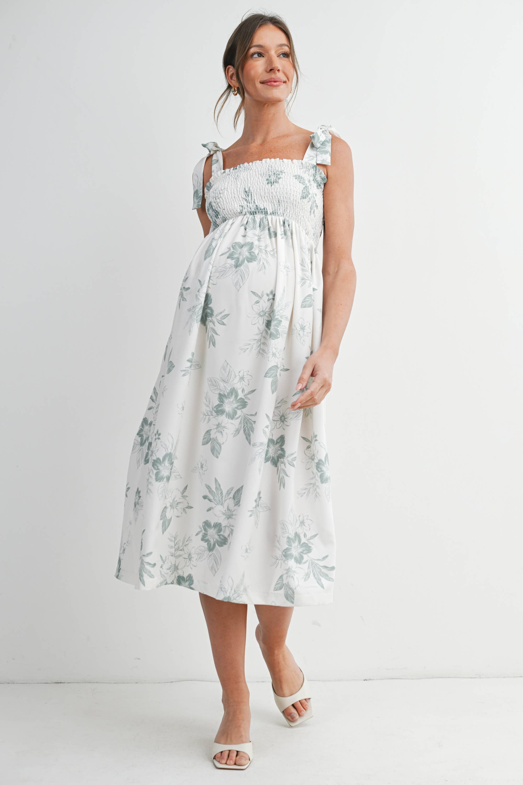 Woman wearing a floral maternity dress against a white background