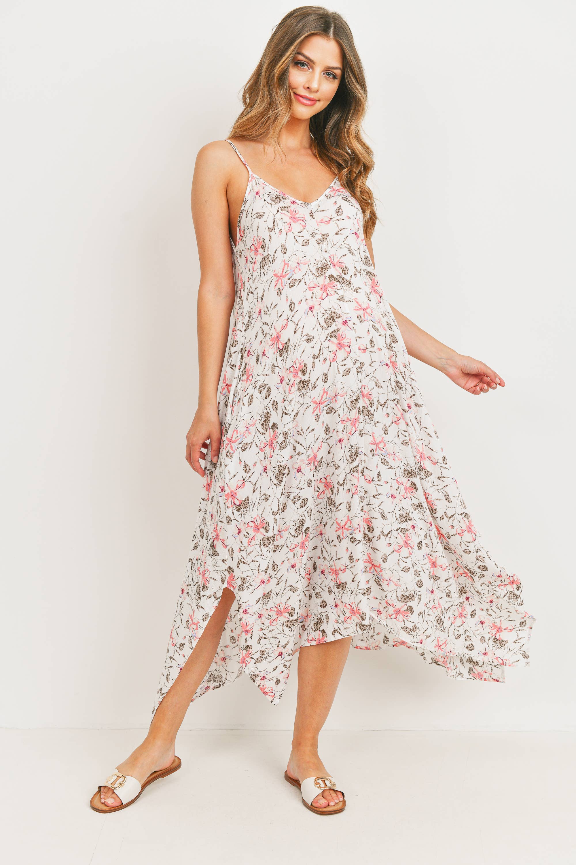 Woman leaning to the right looking at the camera wearing a tropical pink floral  maternity dress on a white background