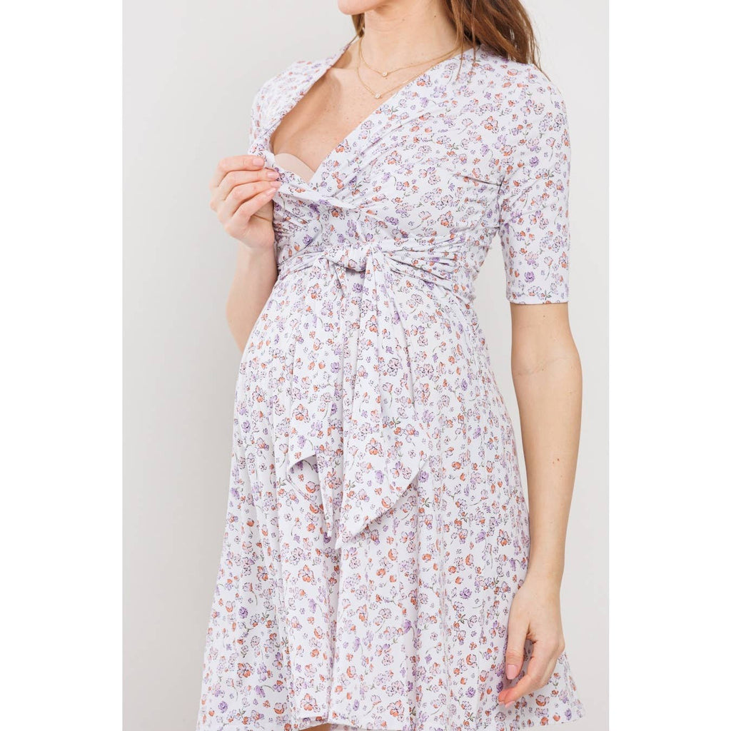 Woman wearing a floral dress against a plain background, her face is out of frame, and she is lifting down the left side of the top part on the dress to showcase that the dress is perfect for breastfeeding